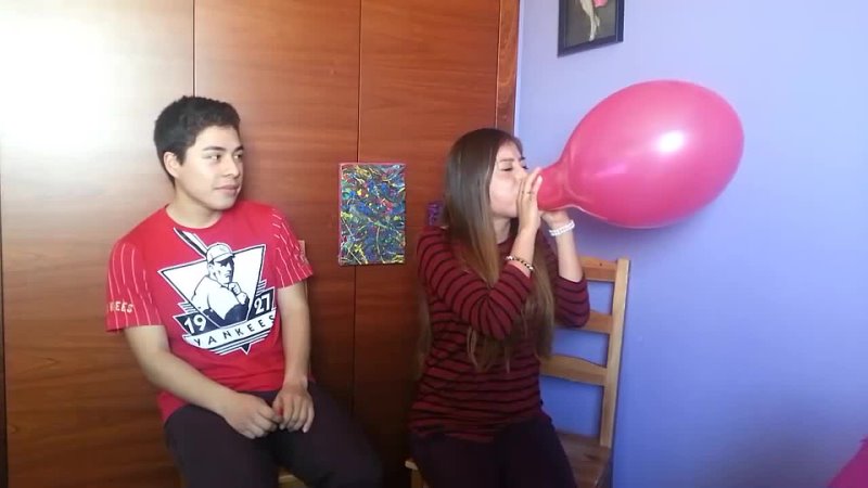 Girl and guy blow to pop red balloon one after
