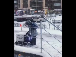 🇷🇺Маленькая девочка счищает снег с робота-доставщика на улице, пока он терпеливо ждет.